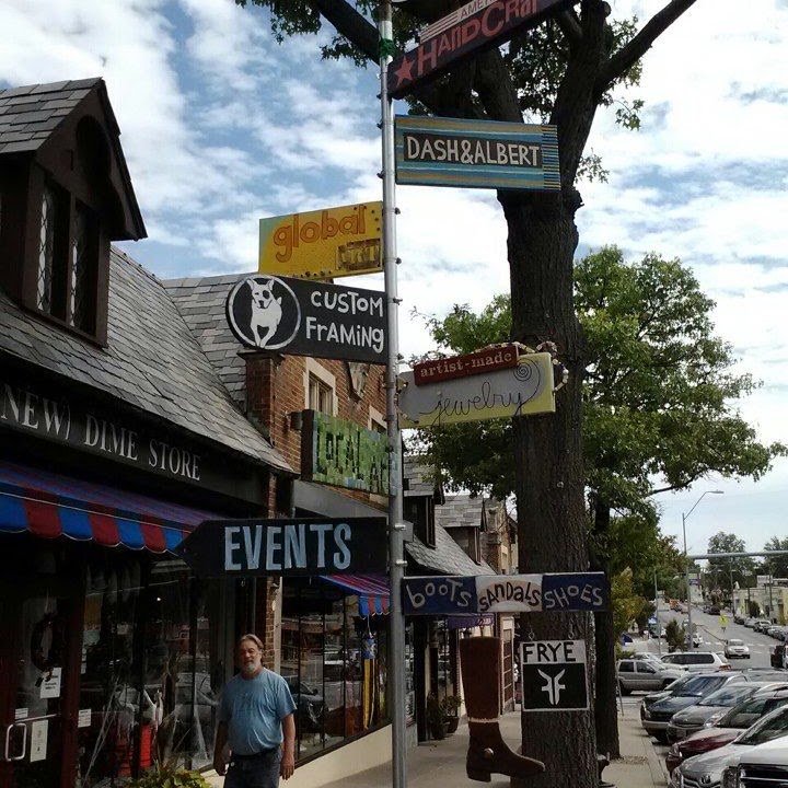 A row of independent shopfronts on a Kansas City street, awnings out, cars parked at the kerb.